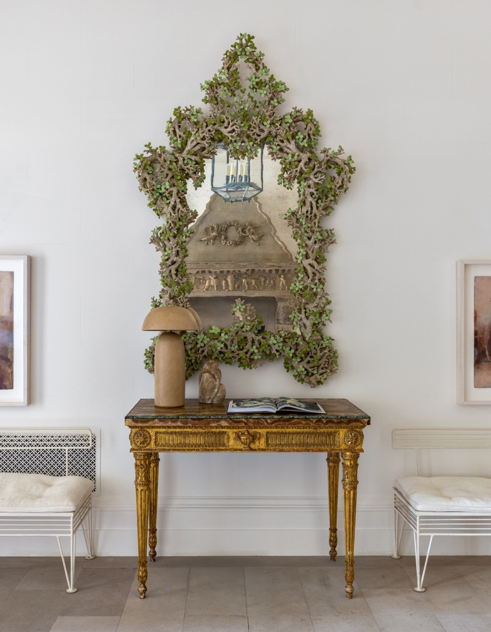 A coral-framed mirror hangs above a giltwood console table topped with a mushroom-shaped lamp