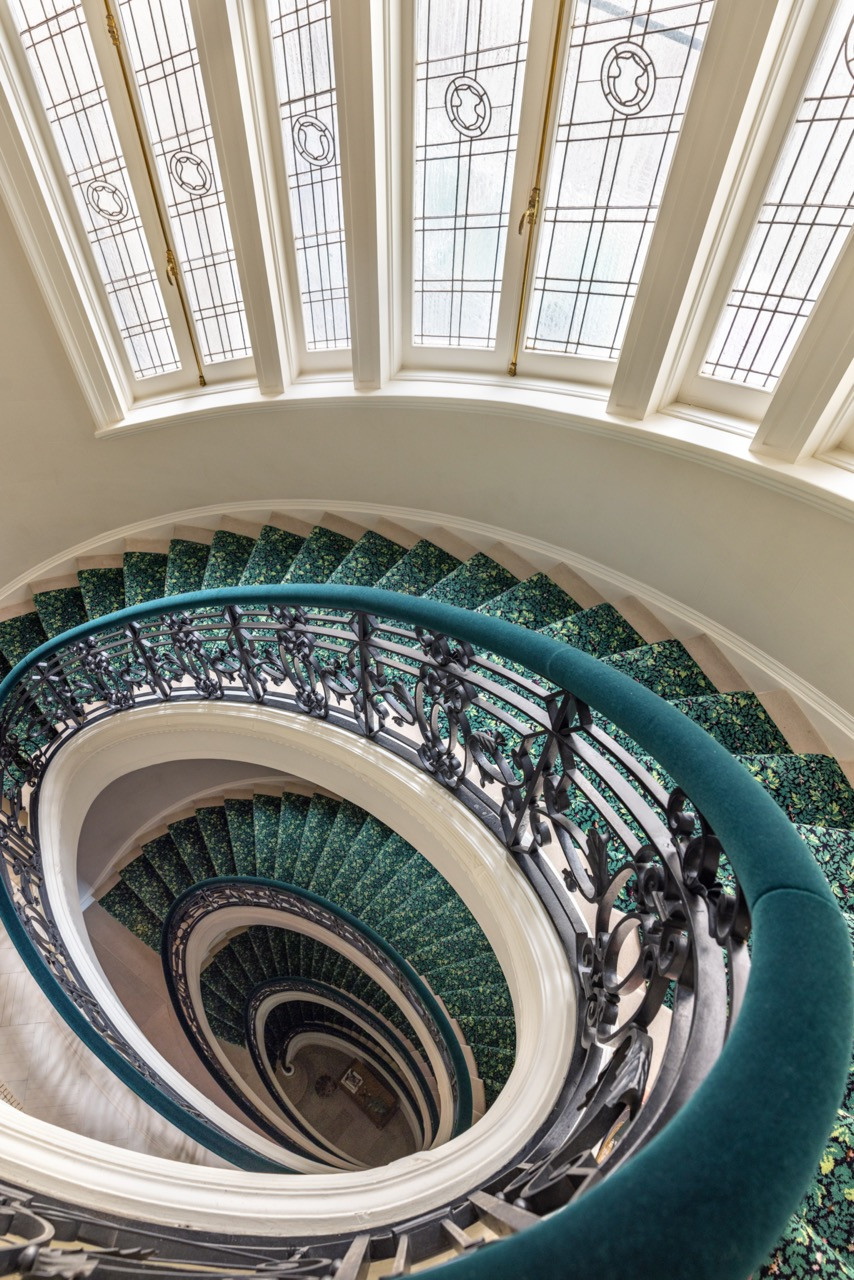 A spiral staircase, its treads carpeted in green, winds beneath a glass-paned oculus