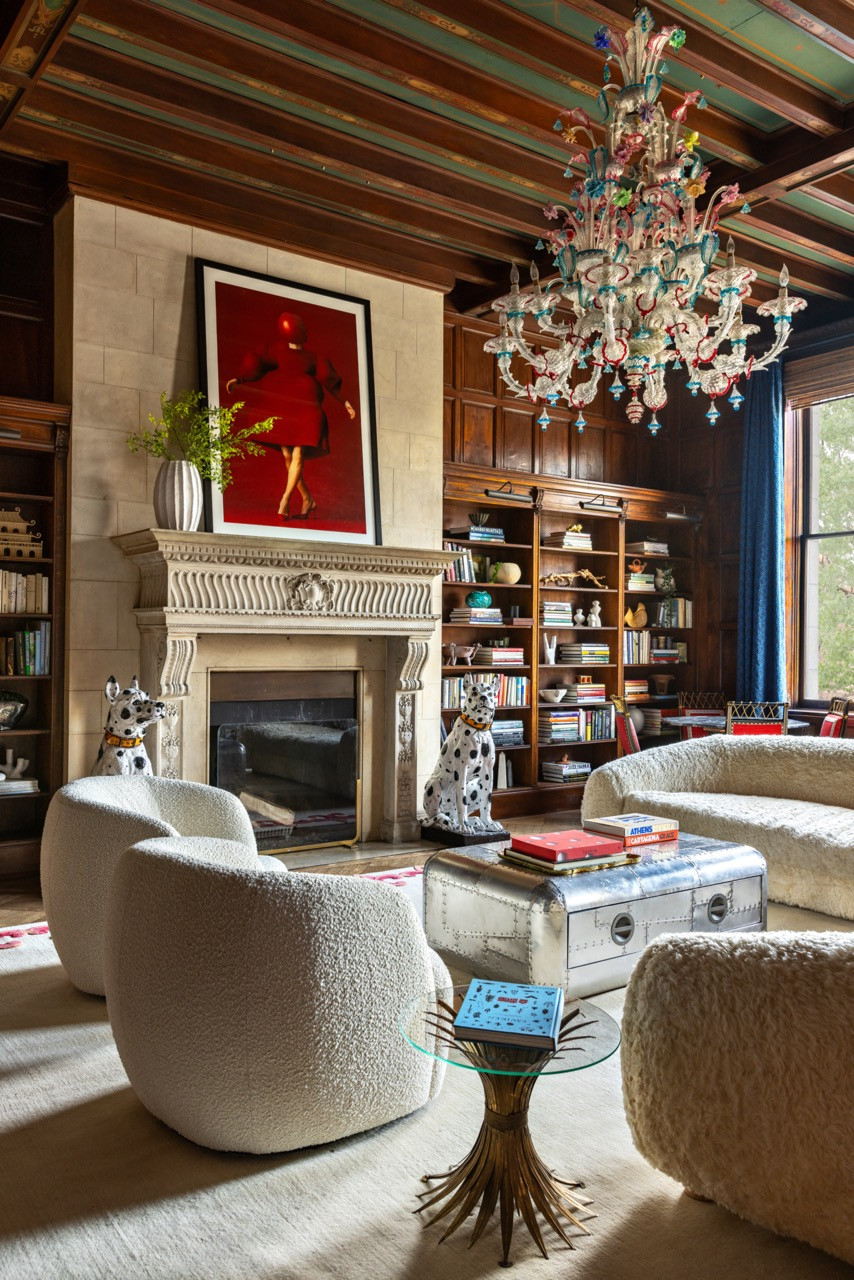 A wood-panelled library holds a Murano glass chandelier, a pair of ceramic Dalmatian statues, and shearling-upholstered seating around a riveted metal trunk