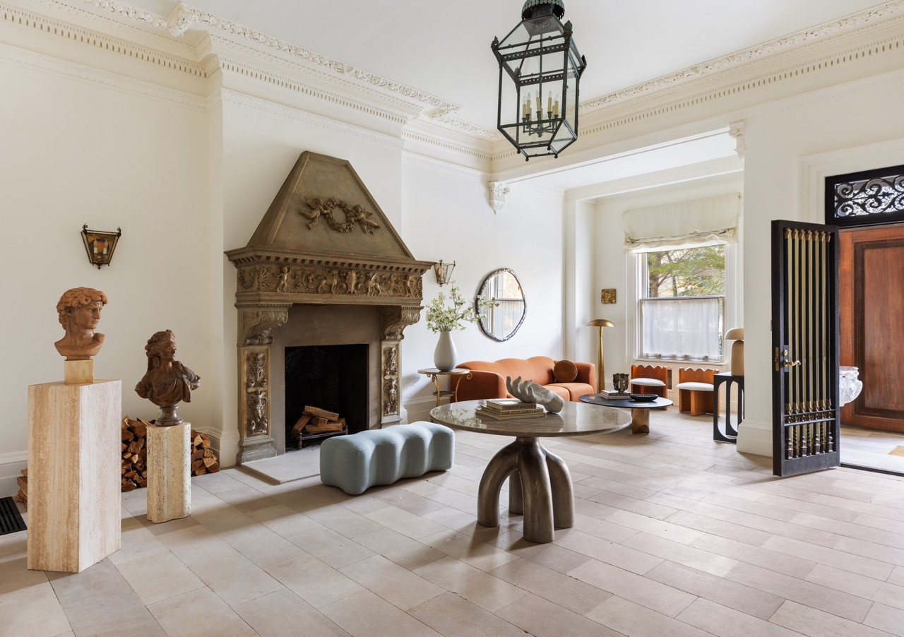 A wide view of the entry room, with its carved fireplace, sculptural busts, and a rust-colored sofa visible through the archway beyond