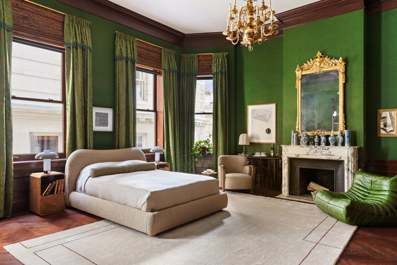 A guest bedroom in emerald green pairs a bouclé bed with a green leather Togo chair beneath a brass chandelier and gilt mirror