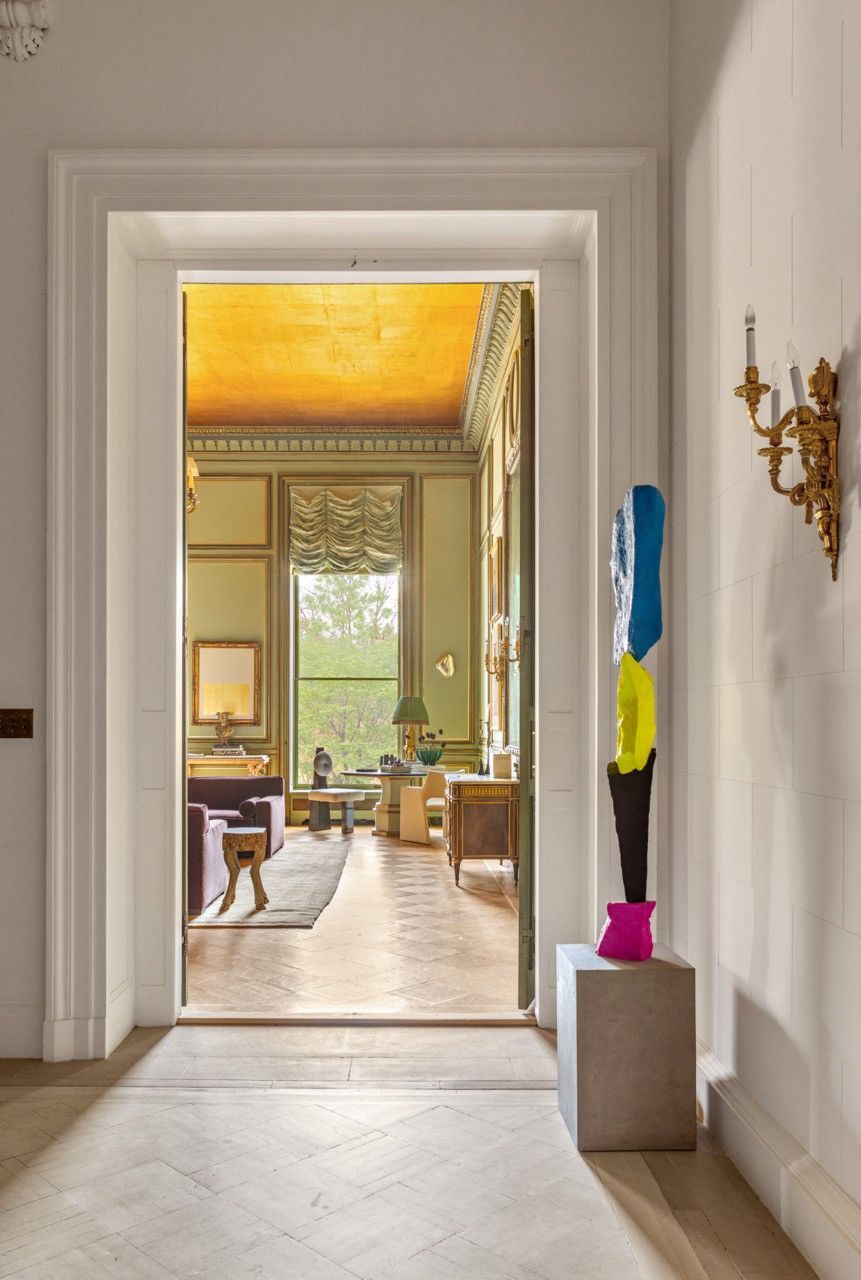 A totem-like painted sculpture stands in a doorway leading into the Green Ballroom, its gilded ceiling visible beyond