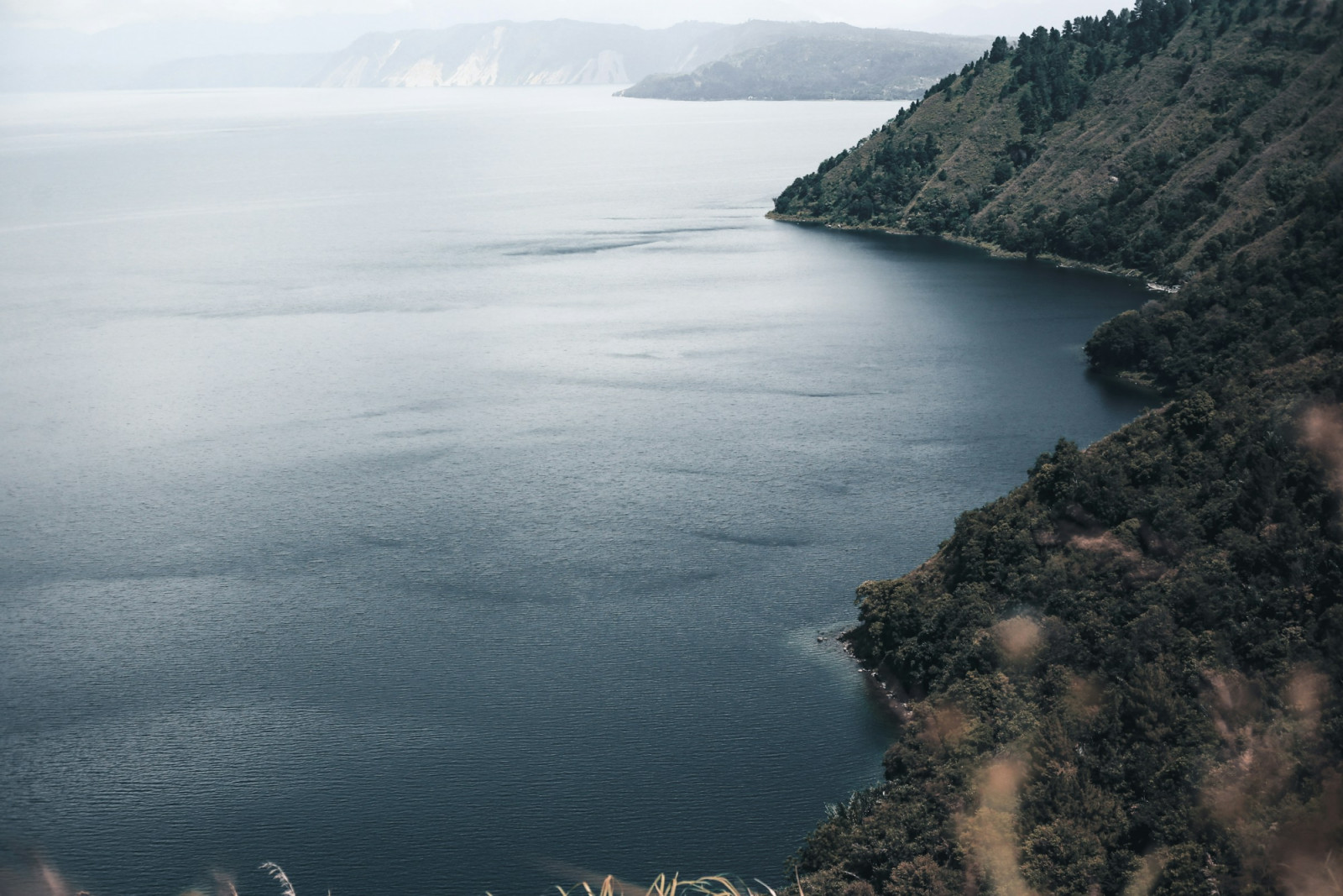 Lush, tree-clad mountains descend to the waters of a vast lake in Asia.
