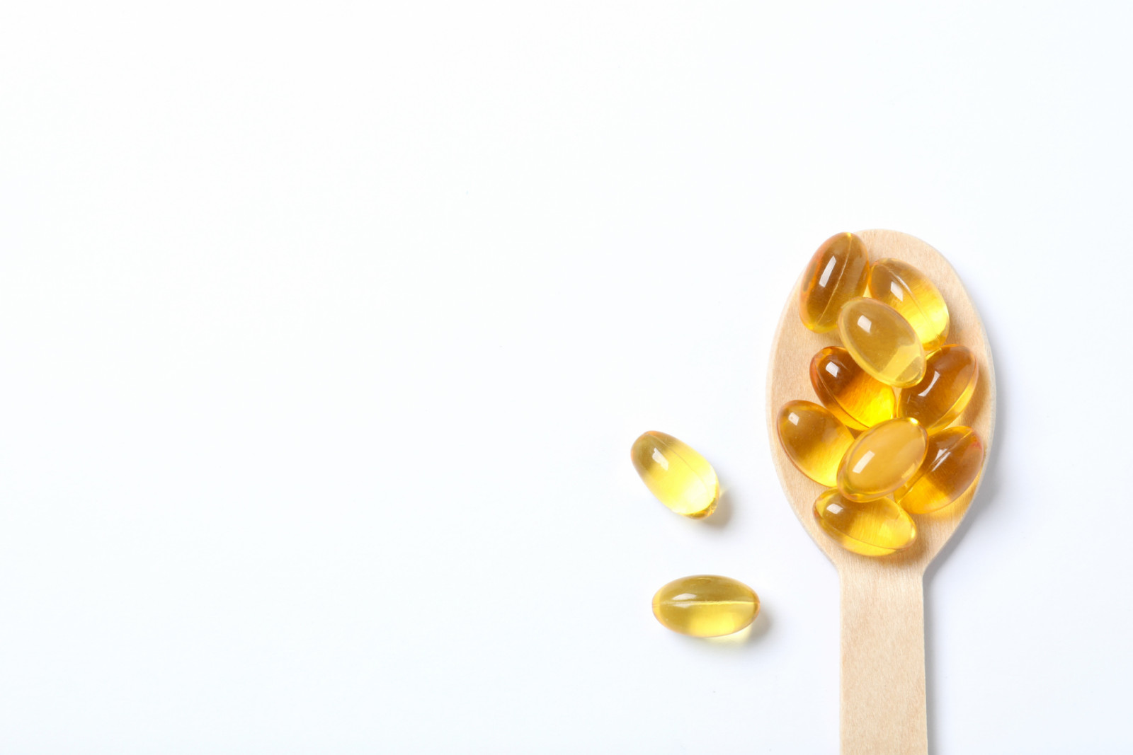 Wooden spoon with capsule of omega 3, 6, 9 fish oil, vitamin, food supplement on white background