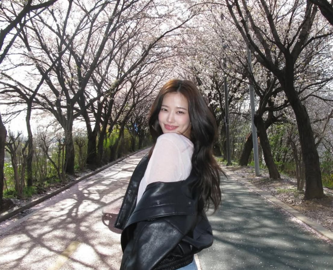 A woman enjoys a sunlit stroll beneath blooming cherry trees.