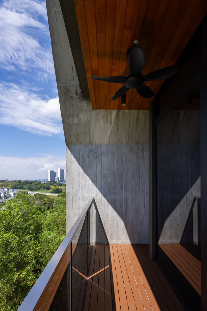 A ceiling fan and timber-lined eave shelter a balcony on an upper floor, where the sloped concrete wall meets a punched window opening