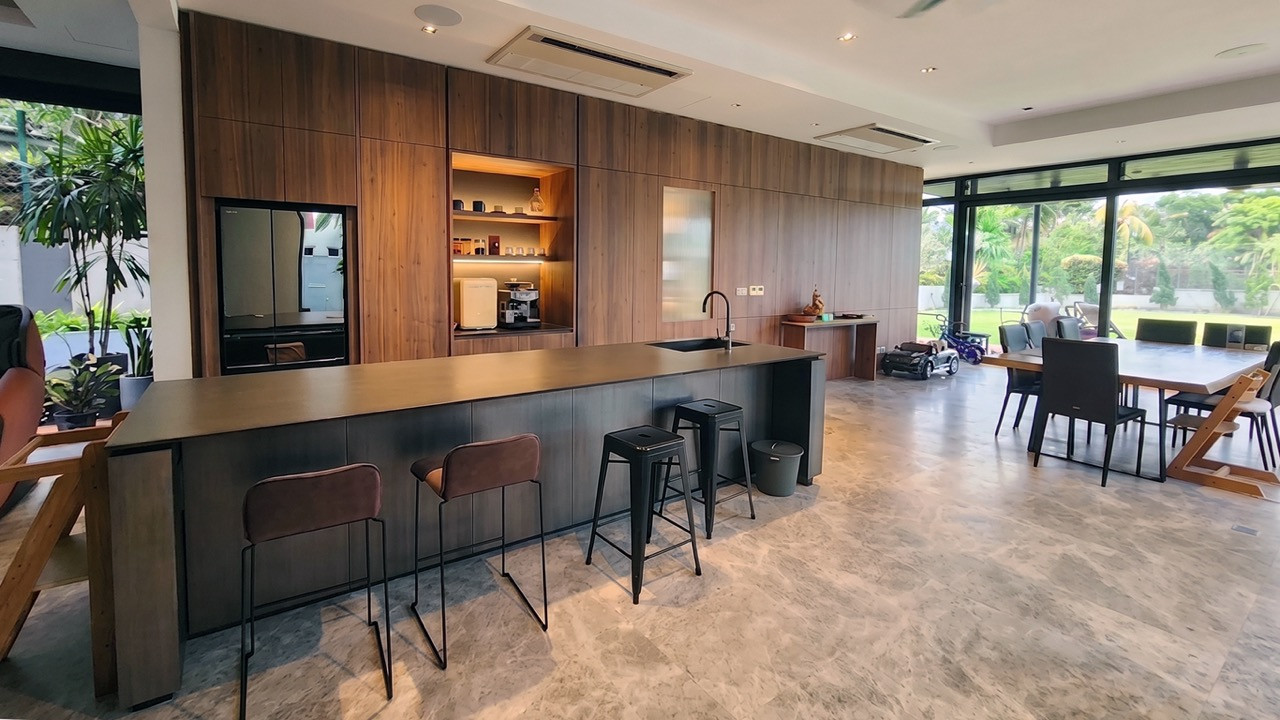 A wood-panelled kitchen island with a bar counter and stools opens onto a dining area and glazed doors leading to the garden.