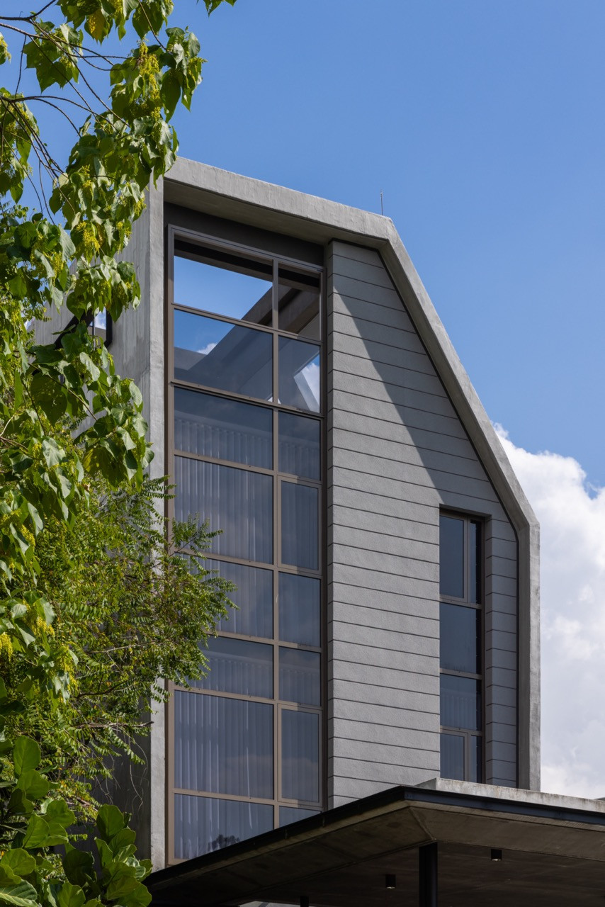 A corner of the upper storey shows the sloped roofline meeting a full-height window bay finished in a ribbed cladding
