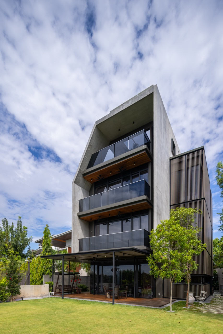 The rear façade shows the house’s stacked balconies, each finished in timber and glass, above a ground-floor terrace opening onto the garden