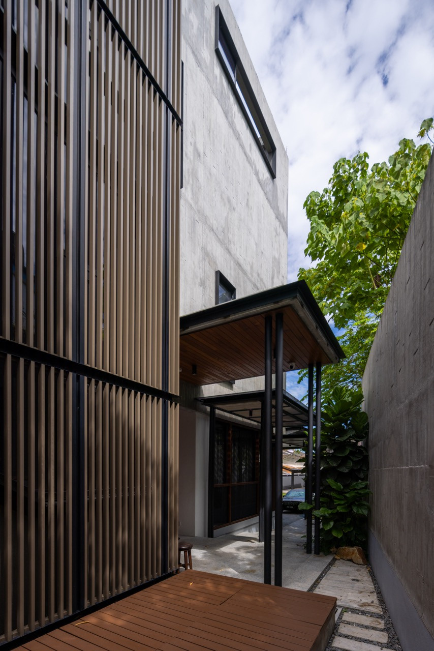 The building’s solid concrete flank meets a lower timber-screened volume, with a covered walkway connecting the twox