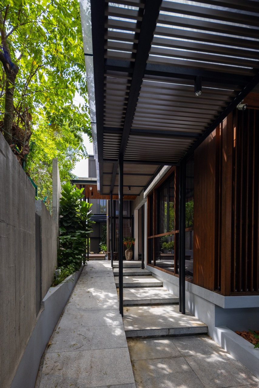 A covered walkway along the side of the house, framed in black steel and timber, leads past full-height glazing.