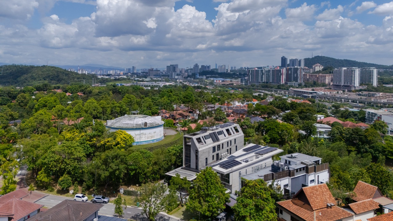 The Kuala Lumpur skyline appears in the distance beyond the house, with its solar panels and folded roofline visible from the air