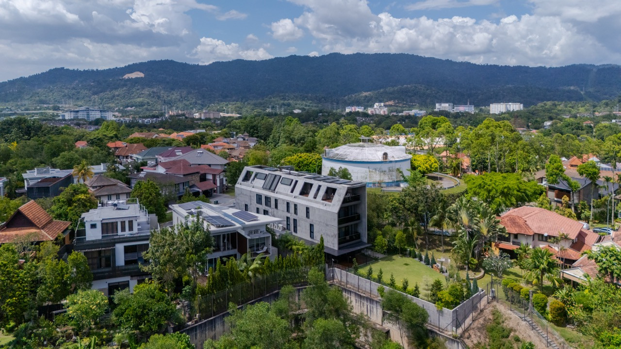 Seen from above, the concrete house sits between a hillside water tank and the surrounding Sierramas rooftops, its sloping upper storeys visible against the tree line