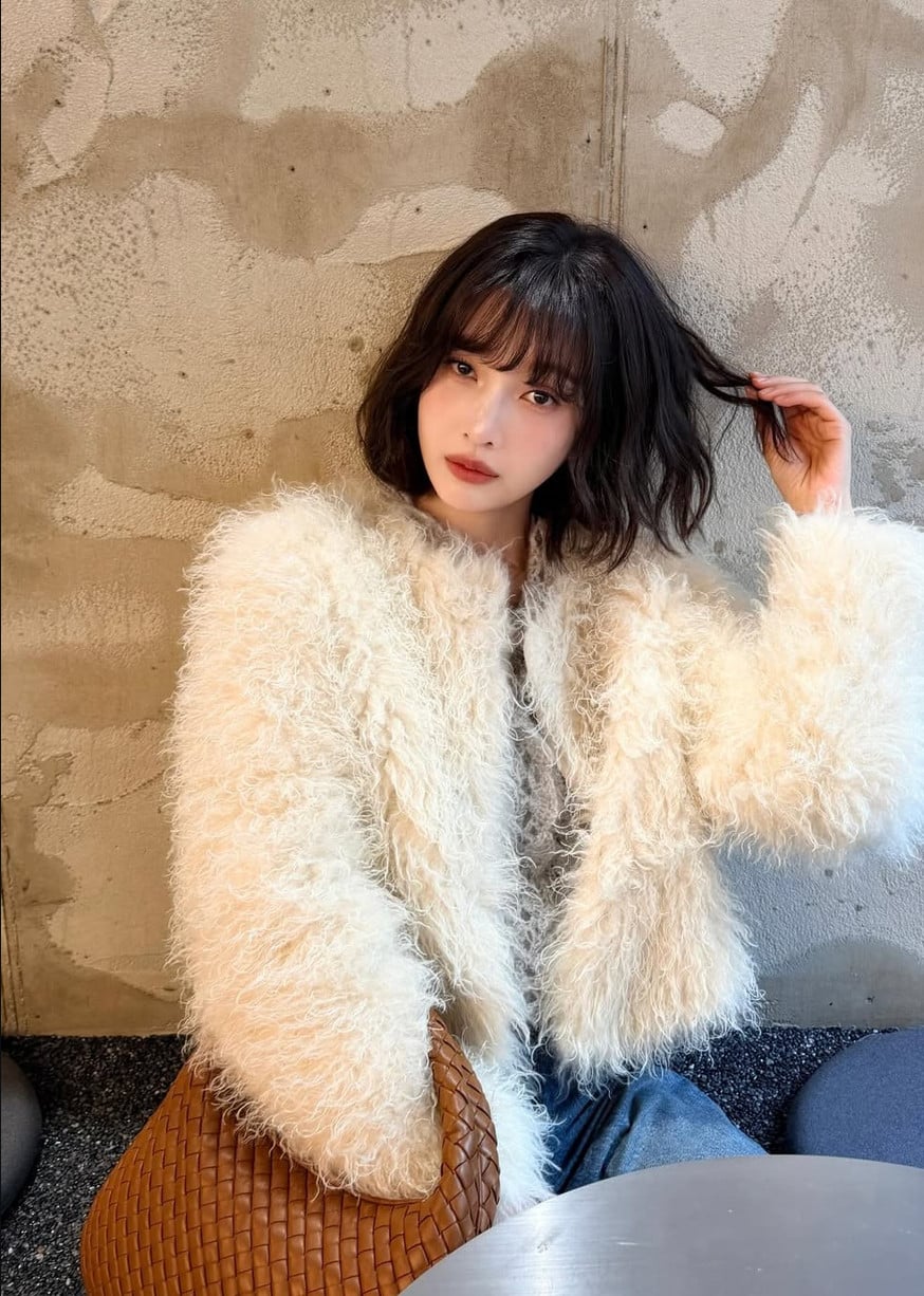 A woman wearing a textured cream jacket, accessorized with a distinctive woven leather bag, embodies effortless luxury.