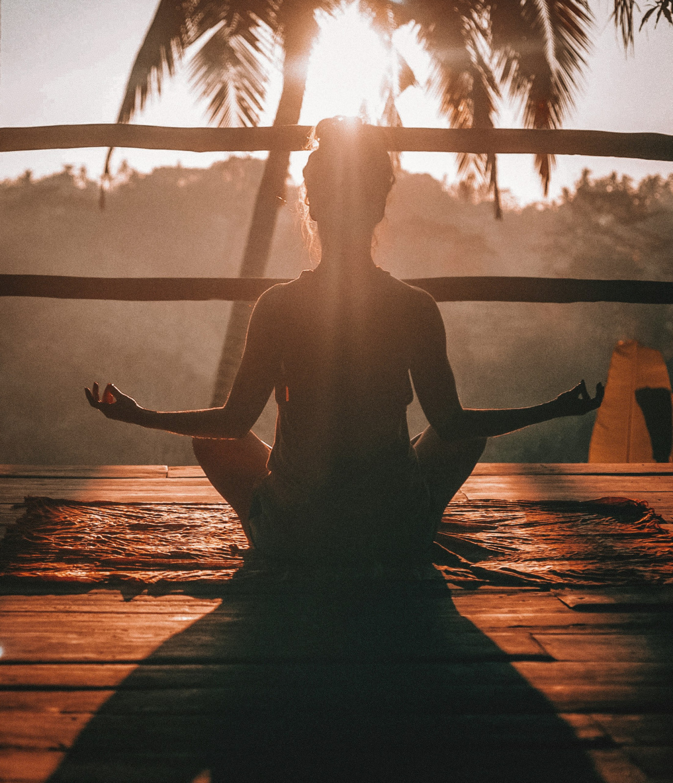 A lone figure finds calm through meditation at sunrise in a tropical landscape.