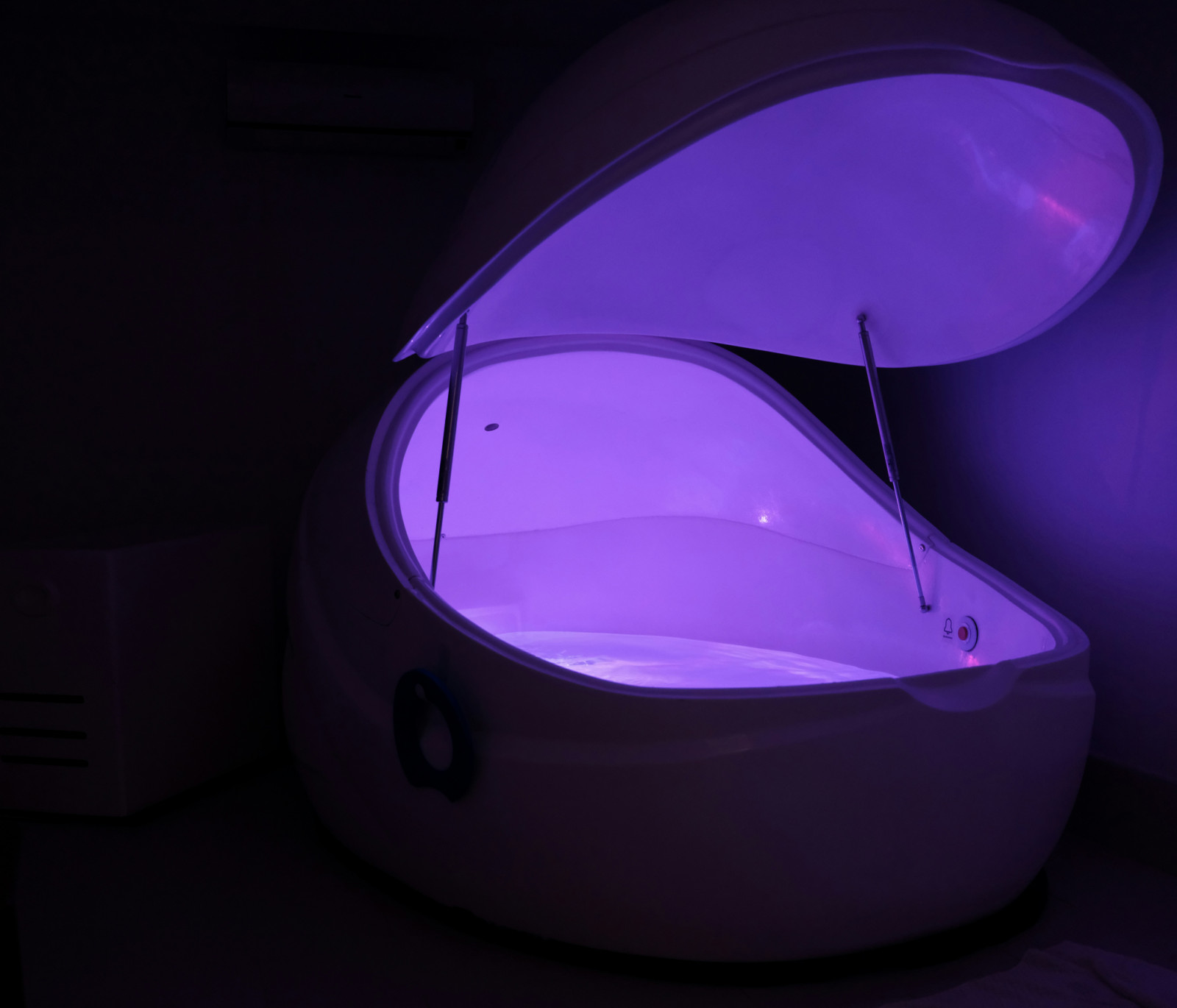 A floatation pod with ambient purple lighting offers a unique sensory deprivation experience for profound relaxation.