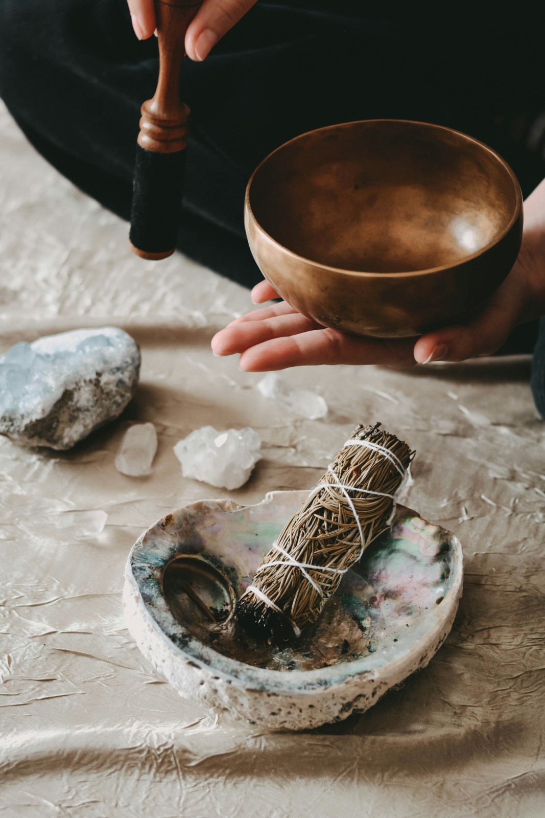 A person prepares a singing bowl, smudge stick, and crystals for mindful meditation and relaxation.