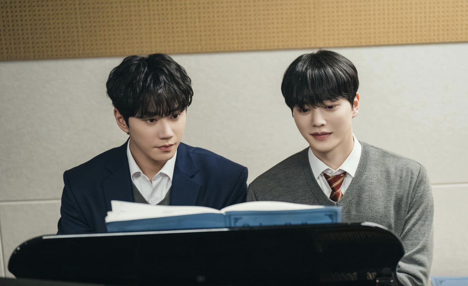 Actors Lee Jun-young and Song Kang are featured in a K-drama scene, seen at a piano with sheet music.