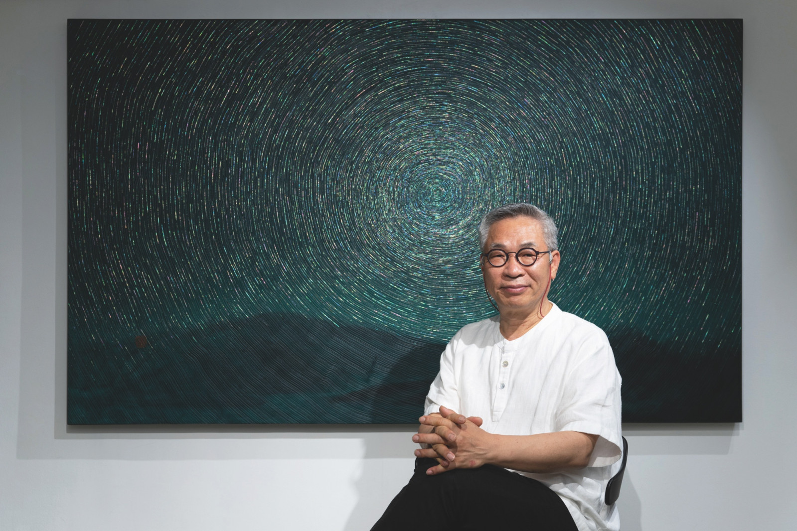 Artist Kim Duck-yong seated in front of his artwork combining iridescent mother-of-pearl inlays with weathered wooden canvases. (Photo: courtesy of Kim Duck-yong)