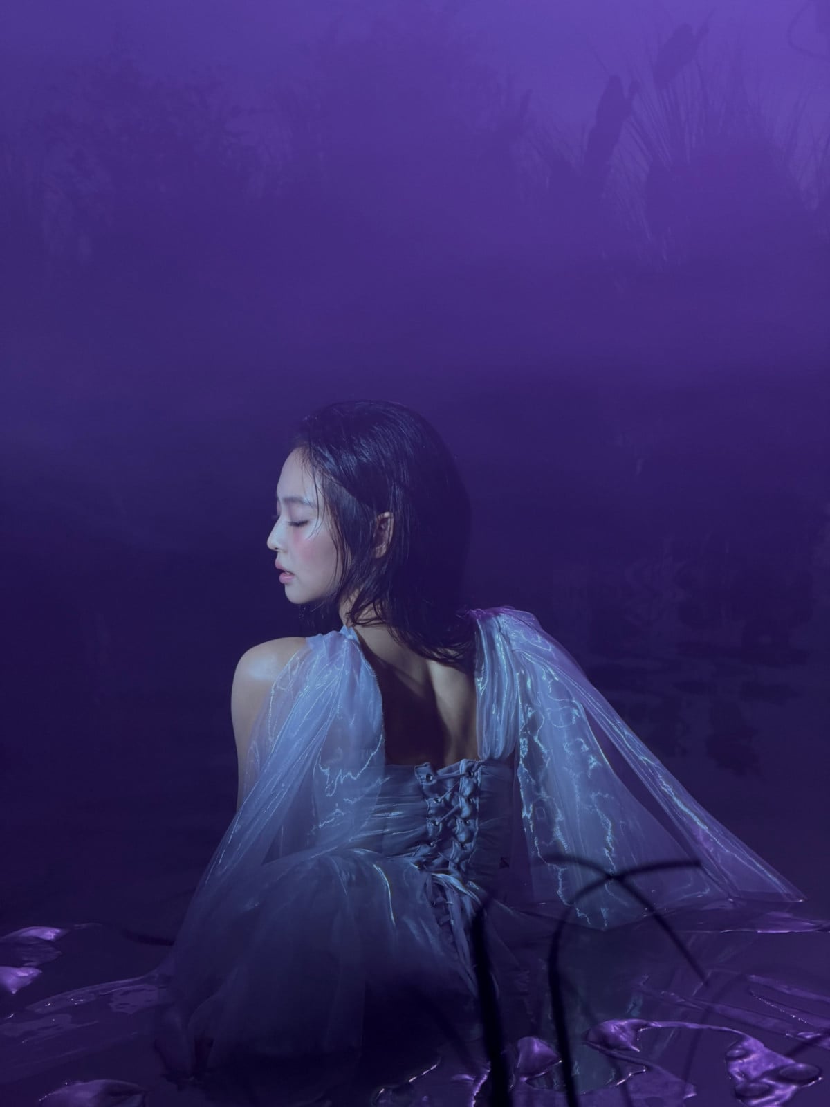 Jennie Kim of BLACKPINK in a delicate, laced gown poses in a purple-hued setting.