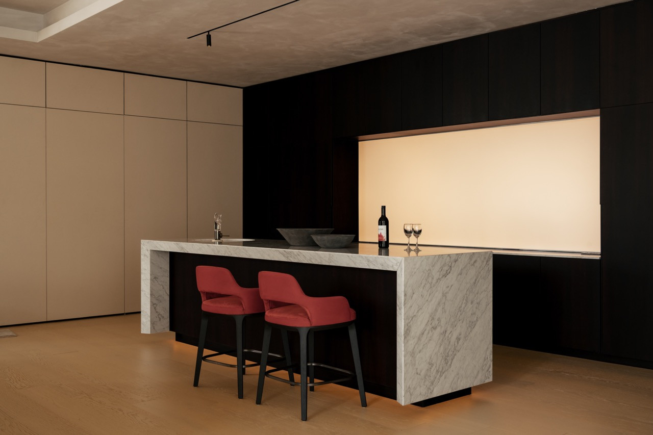 A marble-clad bar counter set against dark cabinetry, with a backlit alcove and red upholstered stools
