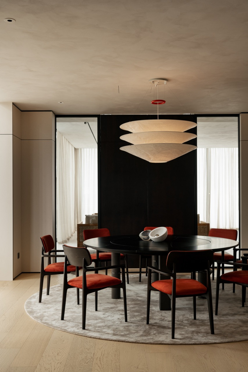 The second dining space features a round black table, red upholstered chairs, and a tiered pendant light against a dark backdrop