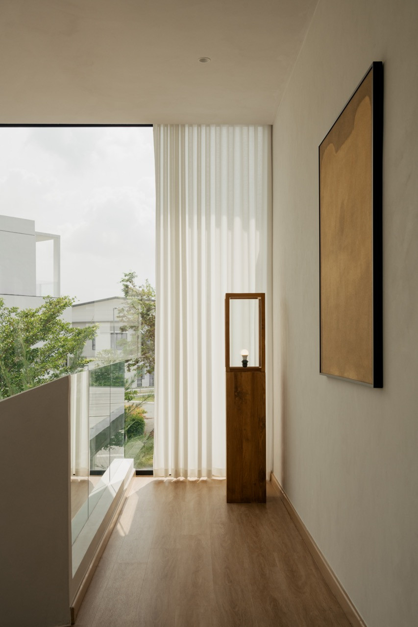 A second-floor hallway with floor-to-ceiling glass, sheer curtains, and a teak-framed accent light beside a framed artwork