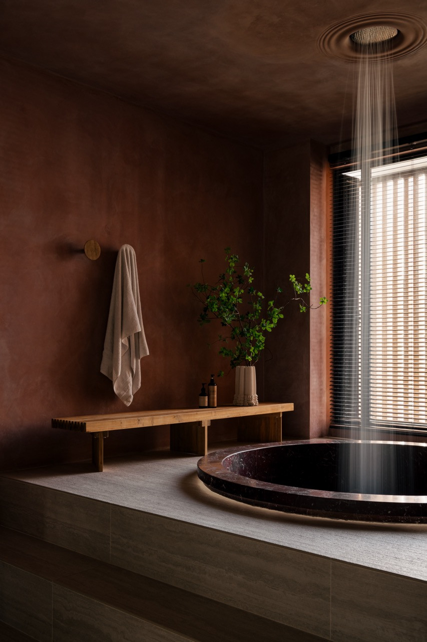 The Rosso Levanto marble bathtub is sunk into a raised platform, with a rain shower positioned directly overhead
