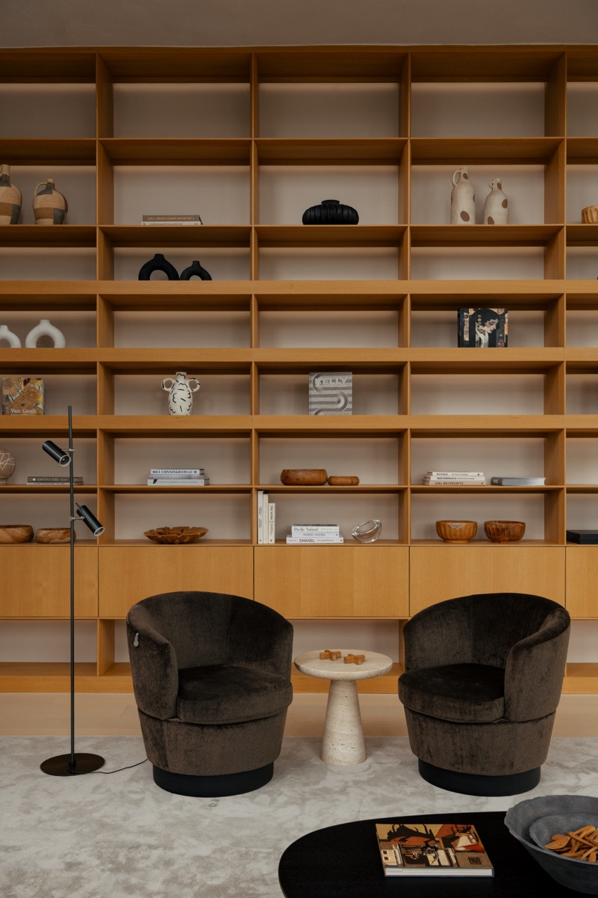 The floor-to-ceiling bookshelf, styled with ceramics and books, with a pair of upholstered swivel chairs set in front