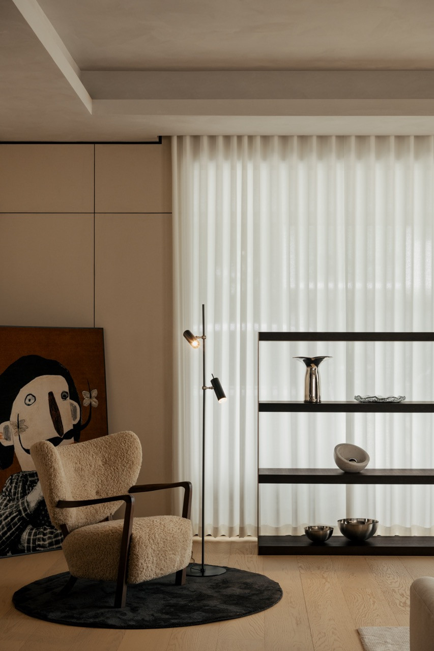 A shearling armchair and floor lamp positioned beside a dark wood shelving unit and framed artwork