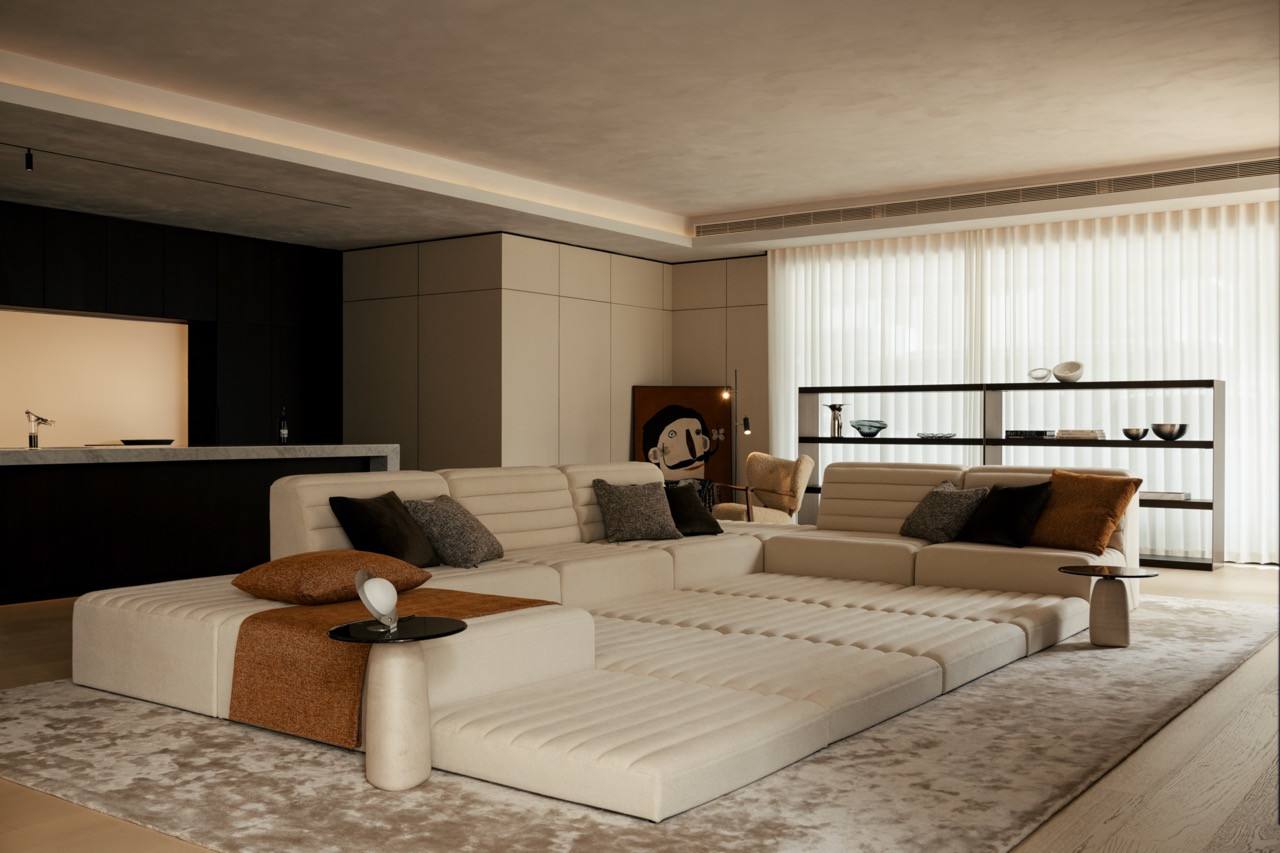 A low sectional sofa anchors the main living area, with the kitchen visible beyond the dark cabinetry
