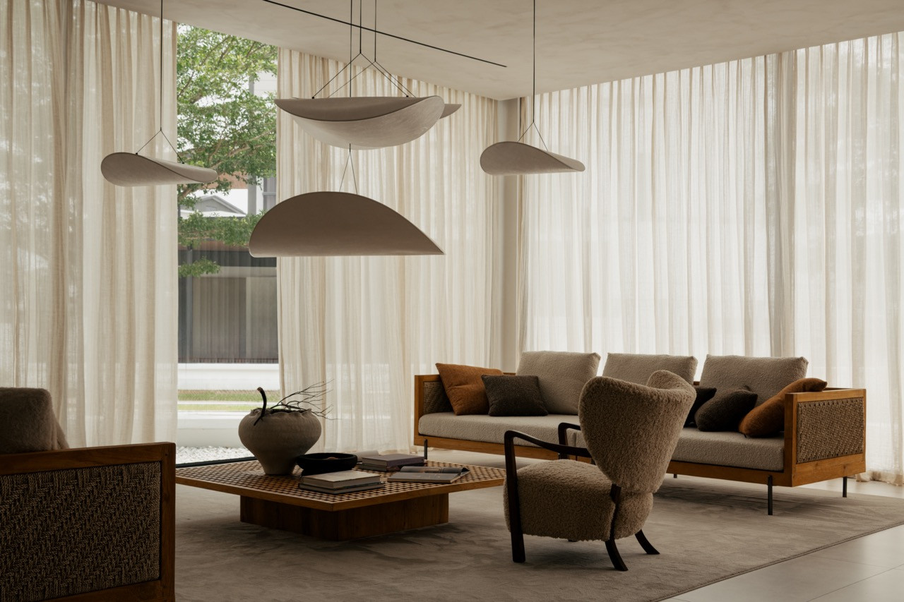 Sculptural pendant lights hang low over the main living area, where a teak-framed sofa and shearling armchair sit beneath sheer curtains