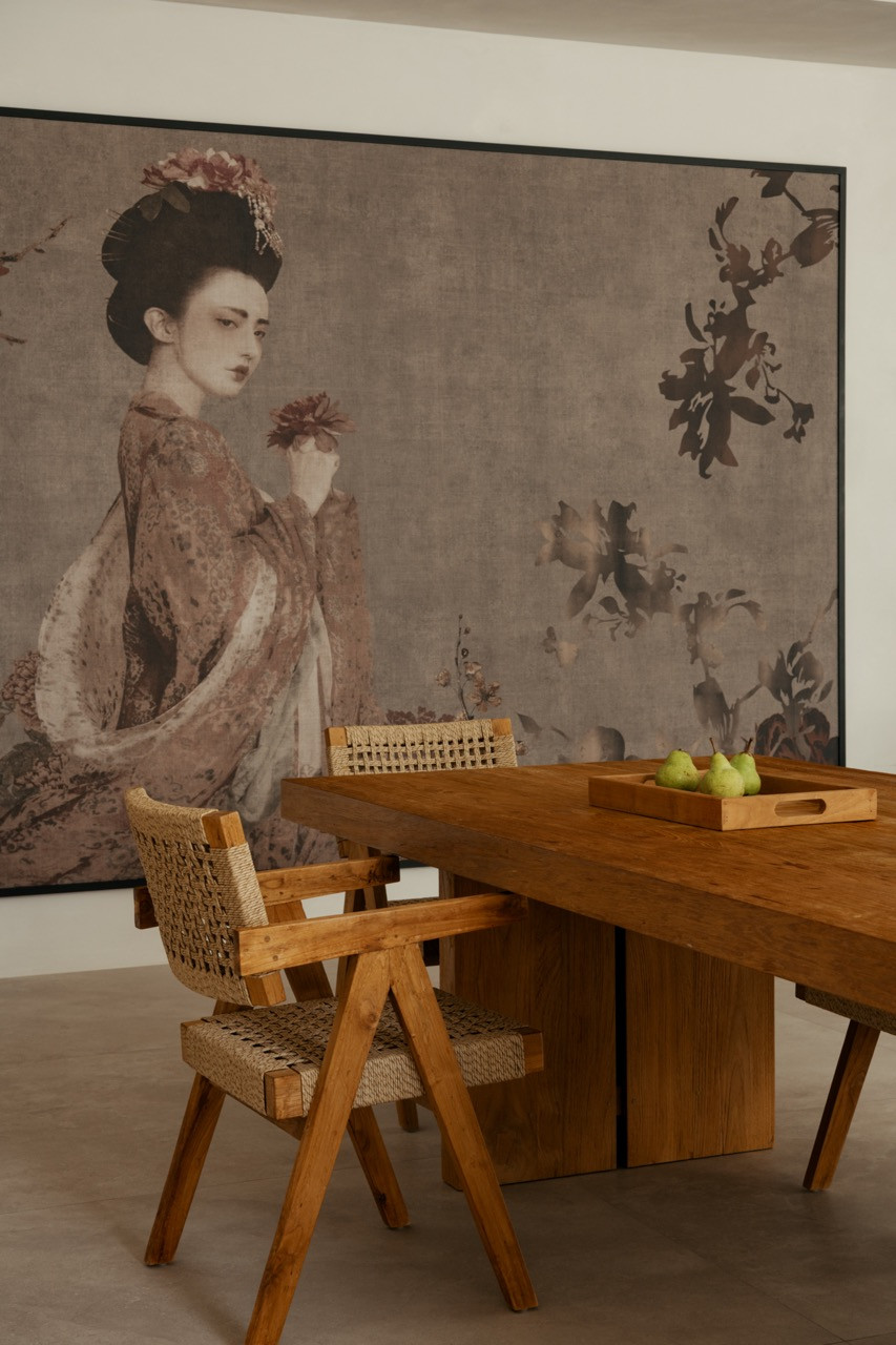 Caos Creativo wallpaper, framed rather than hung flat, behind a teak table and woven armchairs