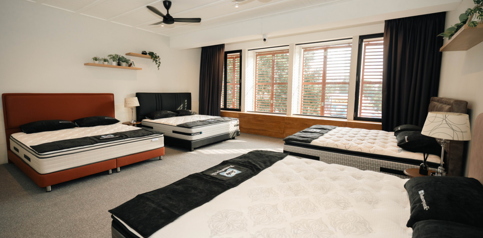A wider view of the display floor, where terracotta and charcoal headboards sit beneath plantation shutters, creating a residential feel rather than a traditional showroom setting