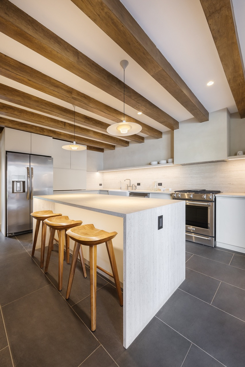 The kitchen, finished with pale stone and exposed beams, was designed with references to traditional Italian farmhouse layouts