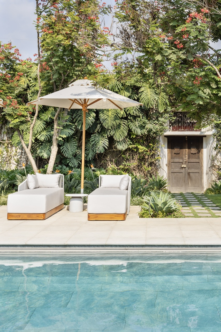 A seating group of green upholstered chairs surrounds a stone fireplace, with sliding glass doors opening the room to the garden