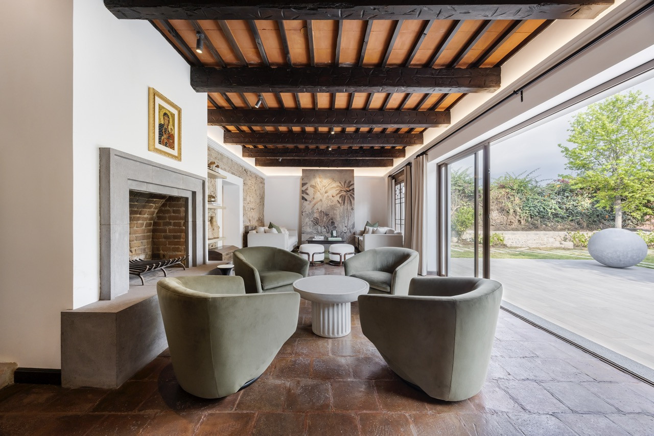 In the kitchen, white cabinetry and a pale stone island sit beneath a beamed ceiling, with the original stone wall visible through the doorway beyond