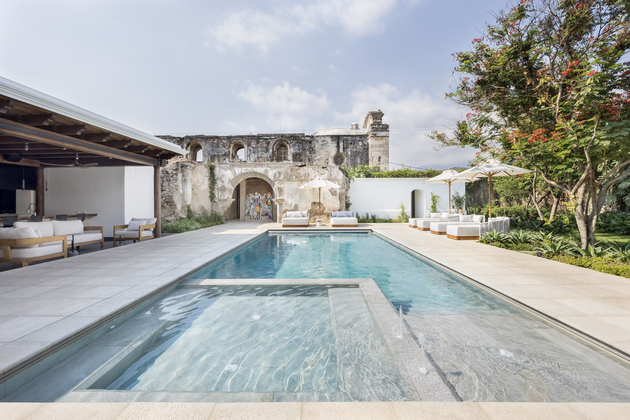 The pool and terrace sit in the shadow of the adjoining ruin, with the mountains visible beyond the garden wall