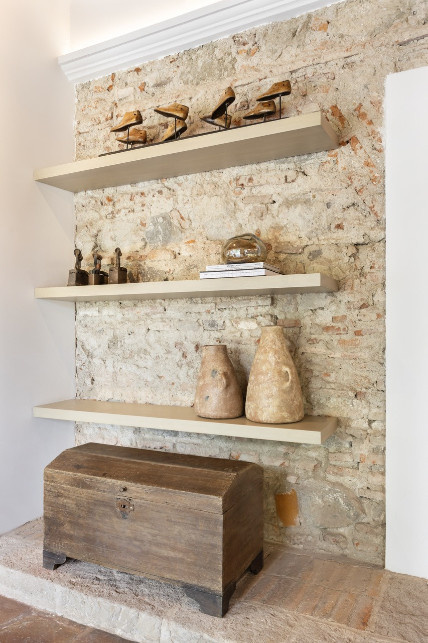 Floating shelves display a collection of antique objects against a section of the home’s original brick and stone