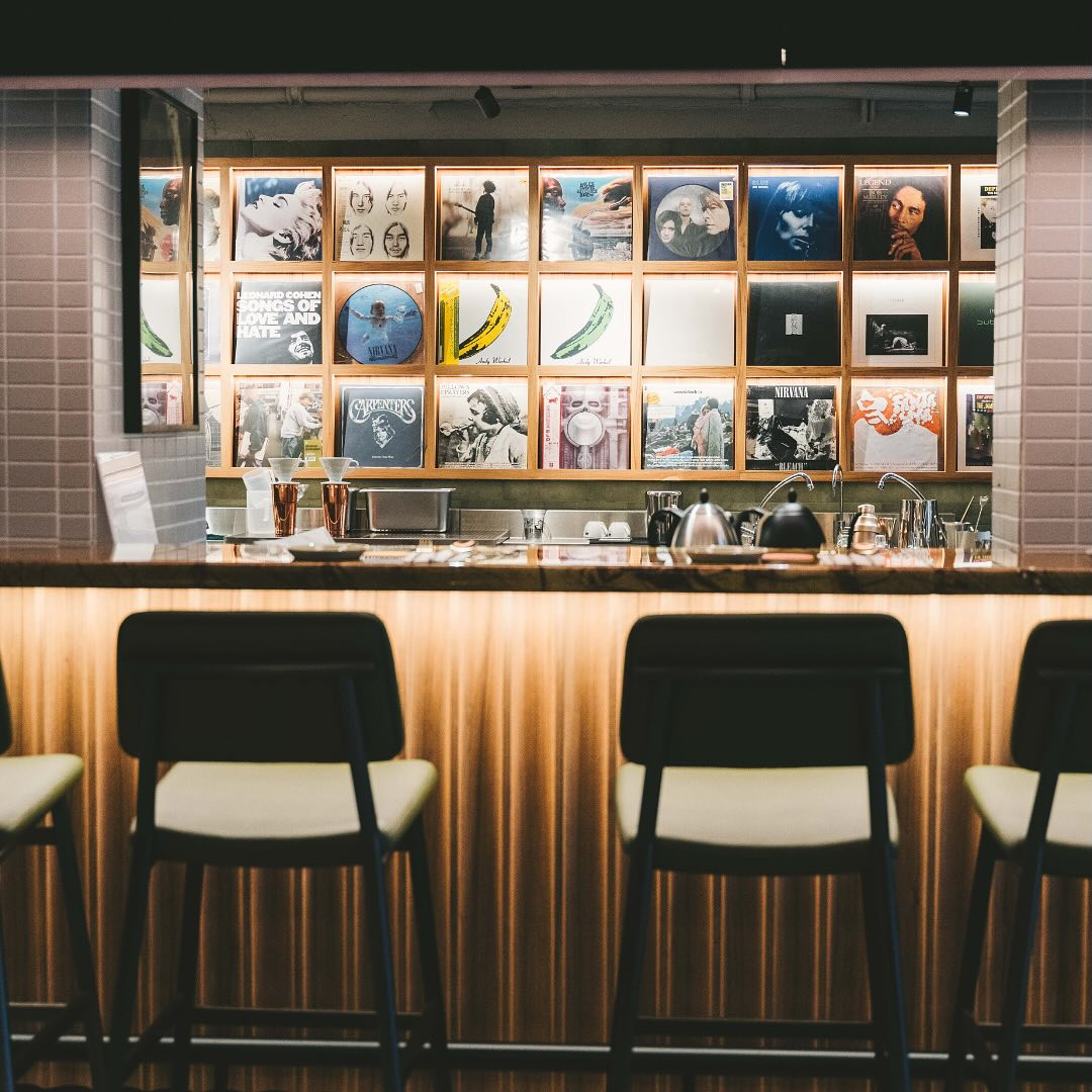 Framed vinyl records, including iconic albums like The Velvet Underground and Nirvana, decorate the wall behind a bar counter.