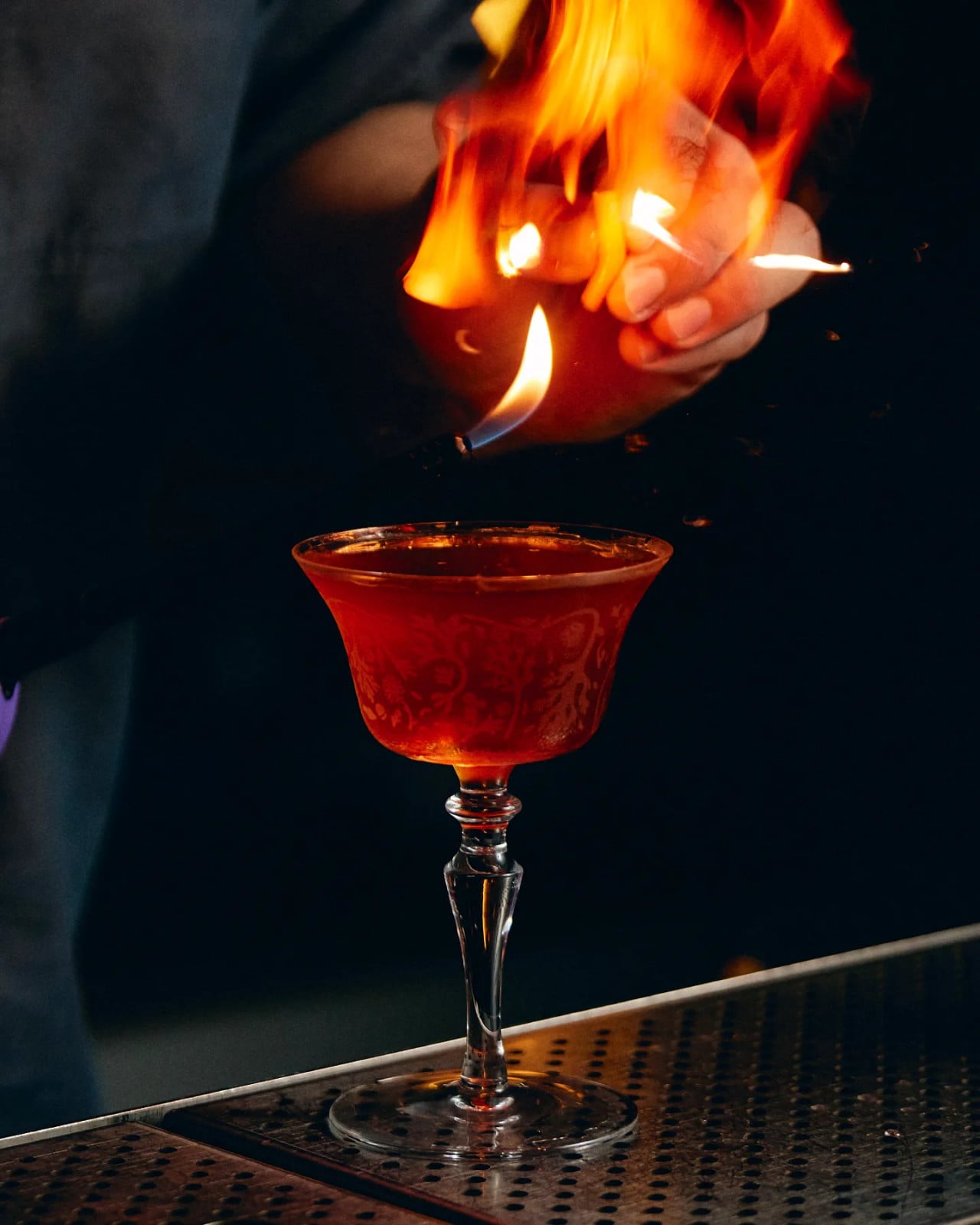 A bartender flames a citrus peel over a cocktail, infusing it with aromatic oils and a dramatic presentation.
