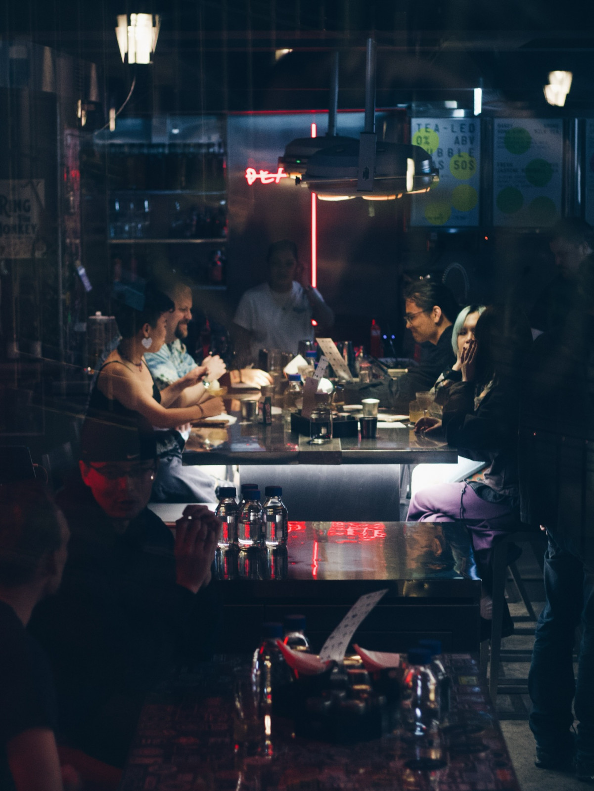 Patrons enjoy drinks and conversation at a modern bar, illuminated by a neon glow.