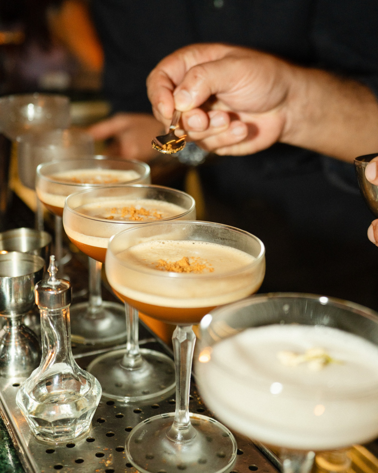 A bartender applies a garnish to several foamy cocktails at the bar.