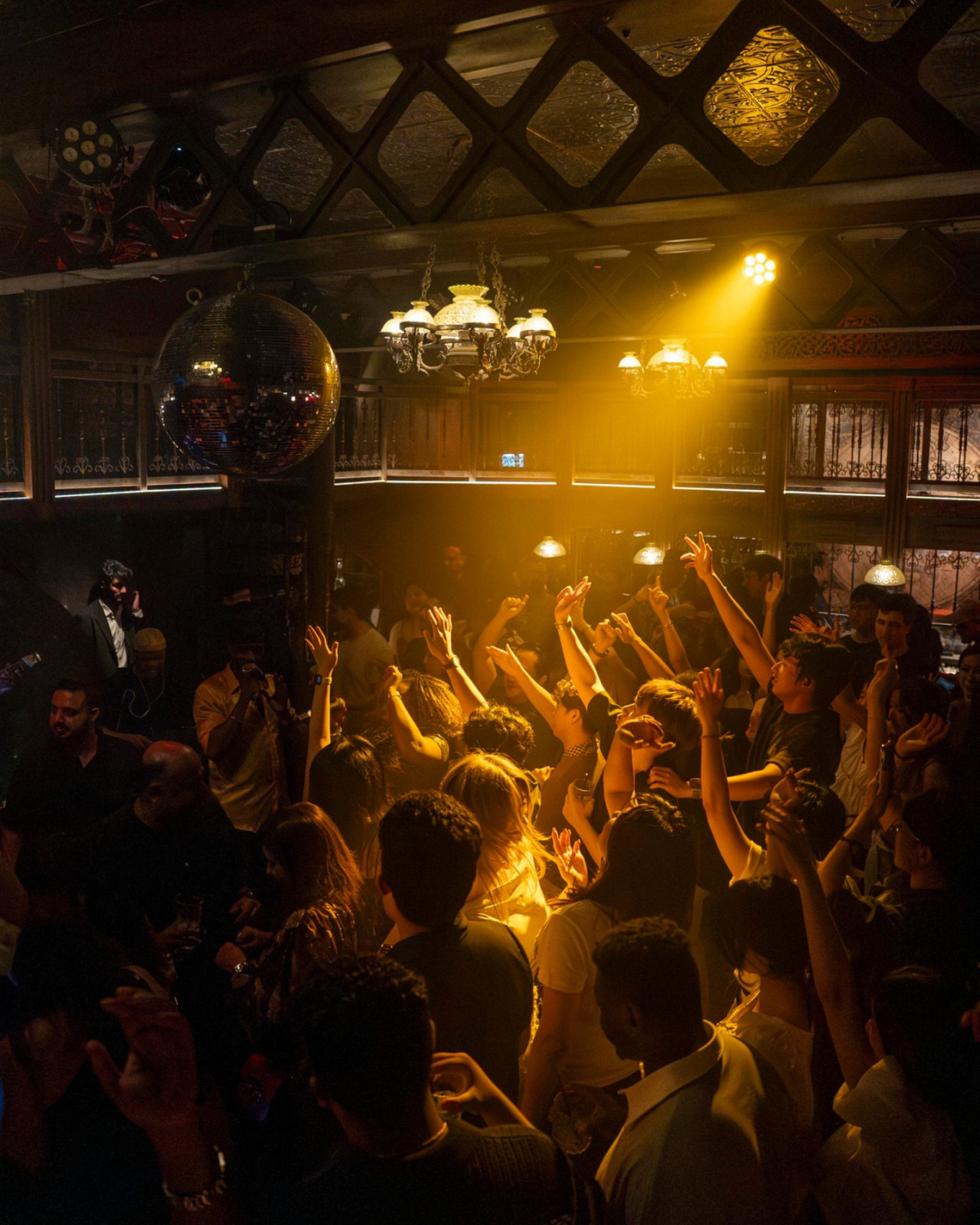 Revelers enjoy an electrifying night, illuminated by a disco ball and spotlights, at a bustling bar.