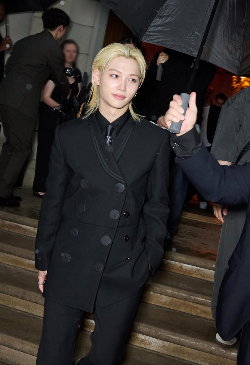 Felix from Stray Kids arrives at an event, wearing a black double-breasted jacket and Louis Vuitton tie.