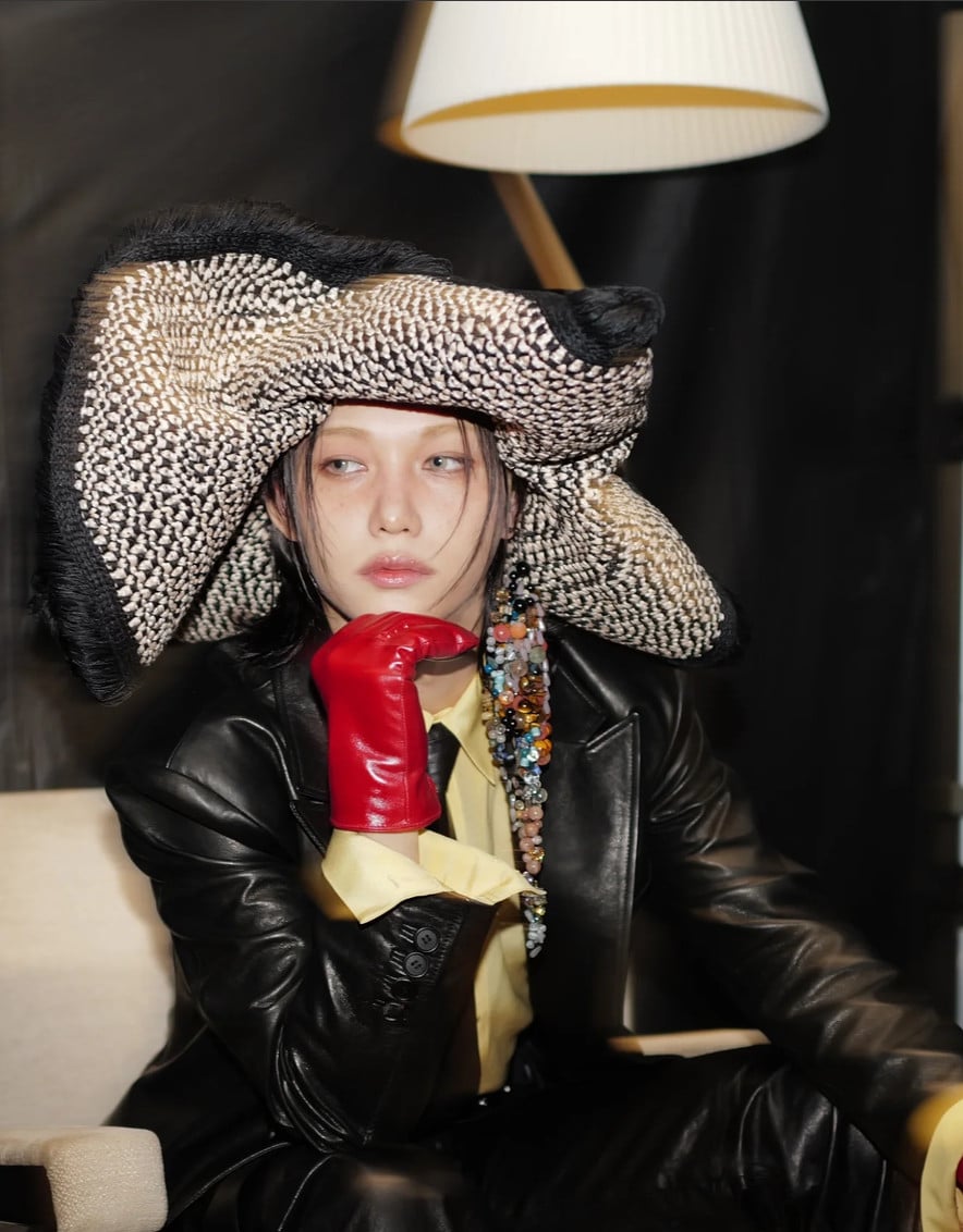 Felix of Stray Kids models a striking patterned hat, black leather jacket, and red glove.