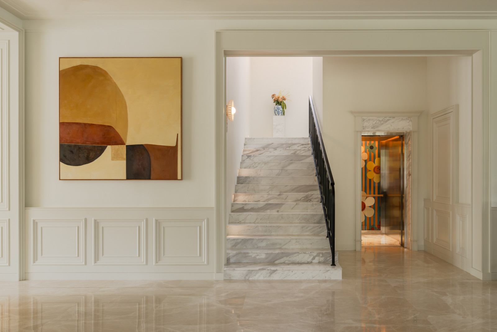 The marble staircase rises beside the home’s lift, its interior papered in a bright floral print, off the main hallway