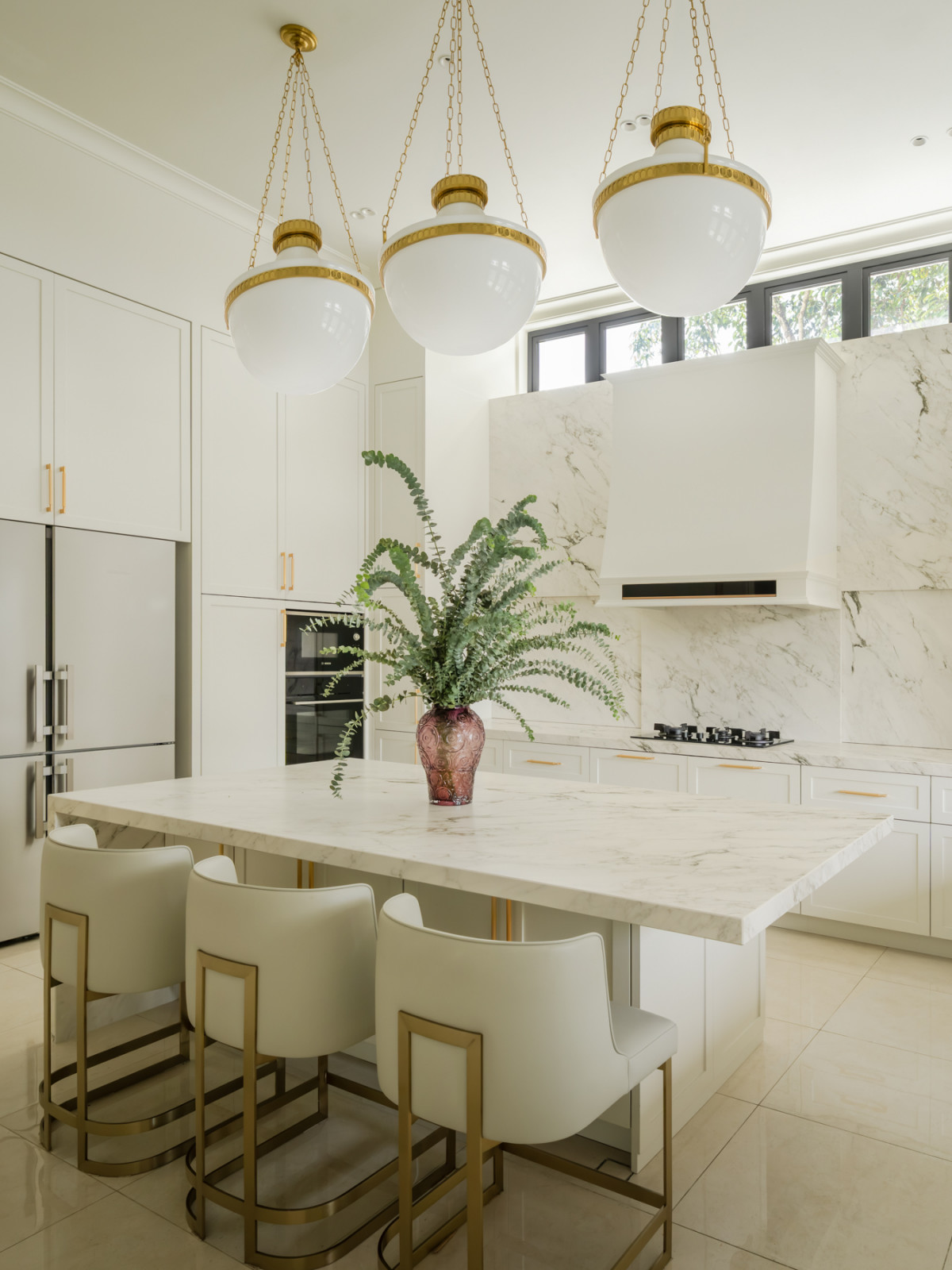 Brass-trimmed globe pendants hang above the kitchen island, with a marble hood over the cooktop behind