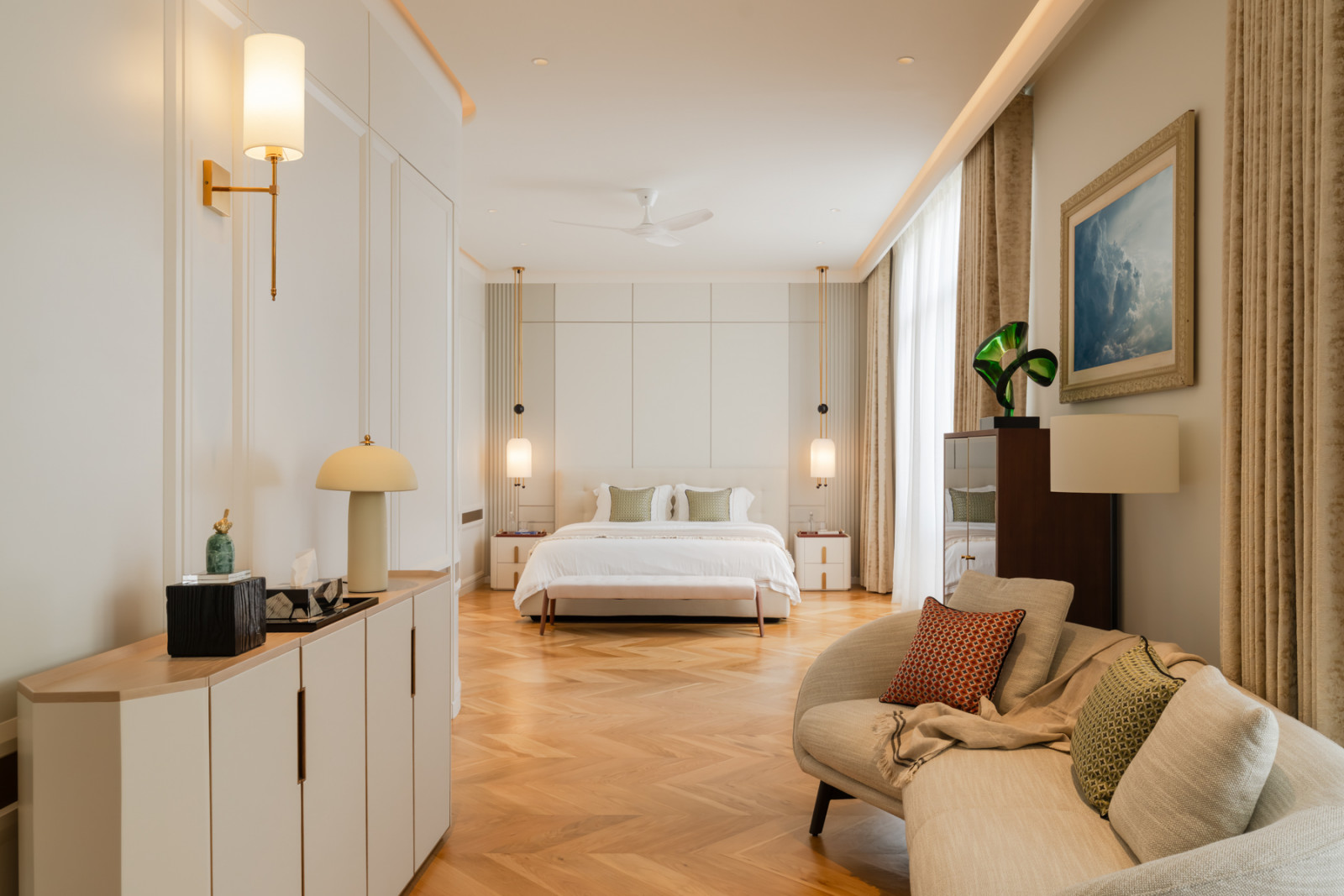 One of the home’s five ensuite bedrooms, furnished with chevron parquet flooring and a pair of pendant lights flanking the bed