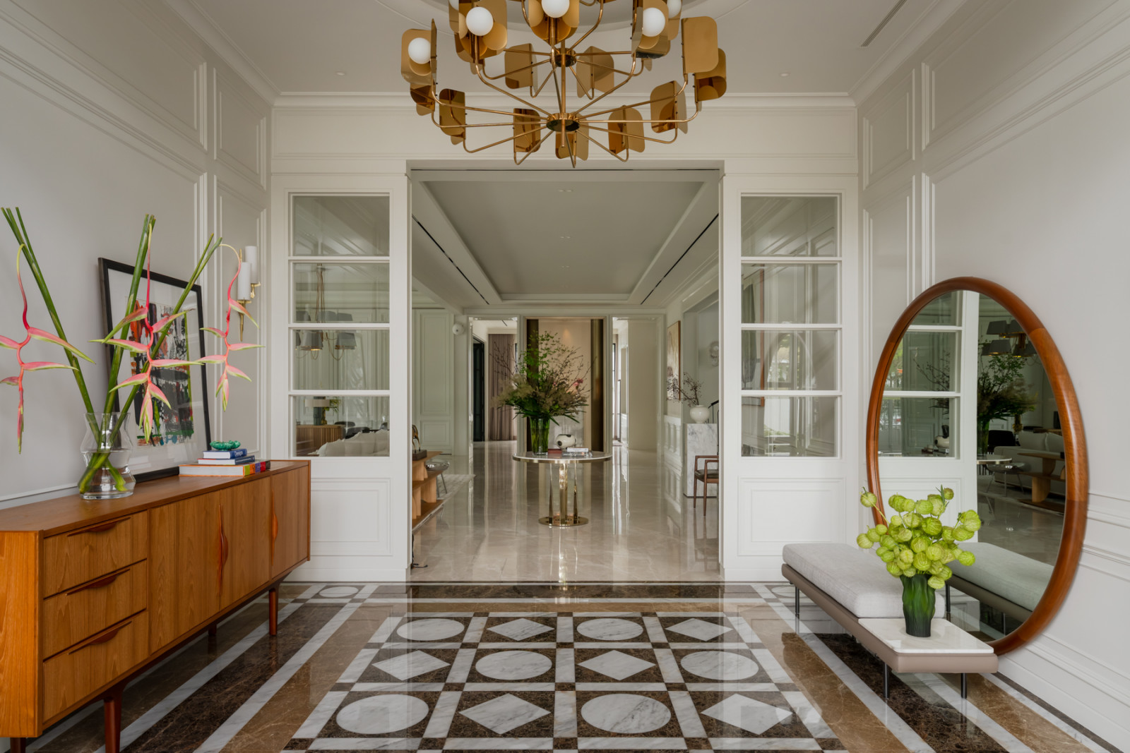 A brass Sputnik chandelier hangs above the foyer, with a vintage sideboard and the round mirror visible on either side of the corridor beyond